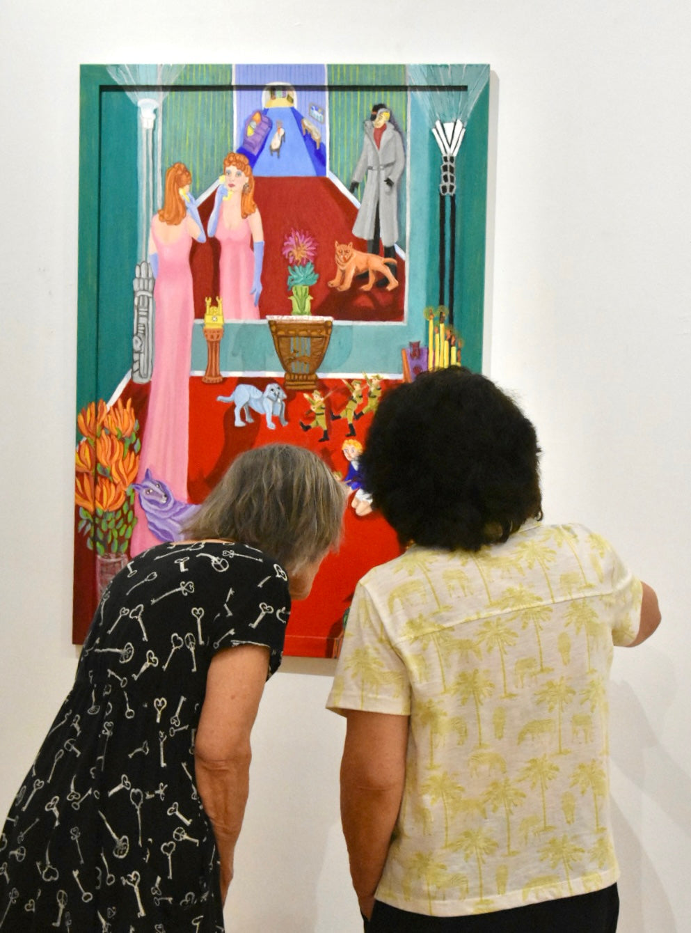Two people looking at a colorful painting of a scene with figures and animals.