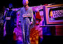 Person in zebra-striped costume with 'APPLAUSE' sign, standing in front of a colorful backdrop with text and props.