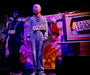 Person in zebra-striped costume with 'APPLAUSE' sign, standing in front of a colorful backdrop with text and props.