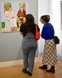 Two people observing a painting in an art gallery.