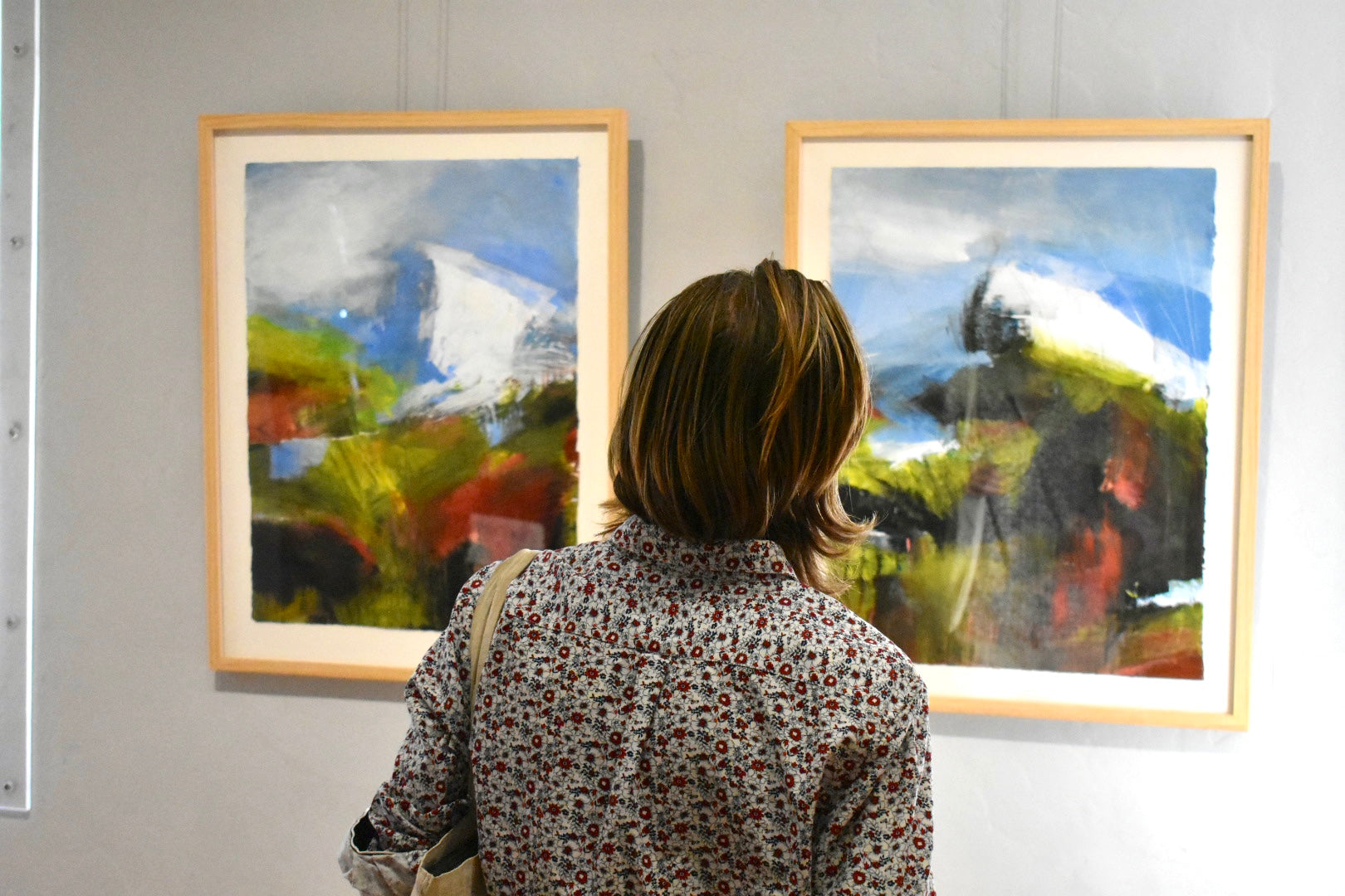 Person looking at two framed paintings of a landscape on a wall.