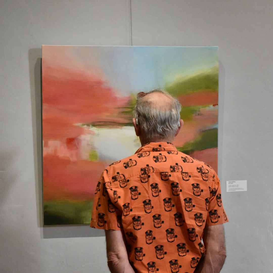 Person holding an orange patterned fabric in front of a colorful abstract painting on a white wall.